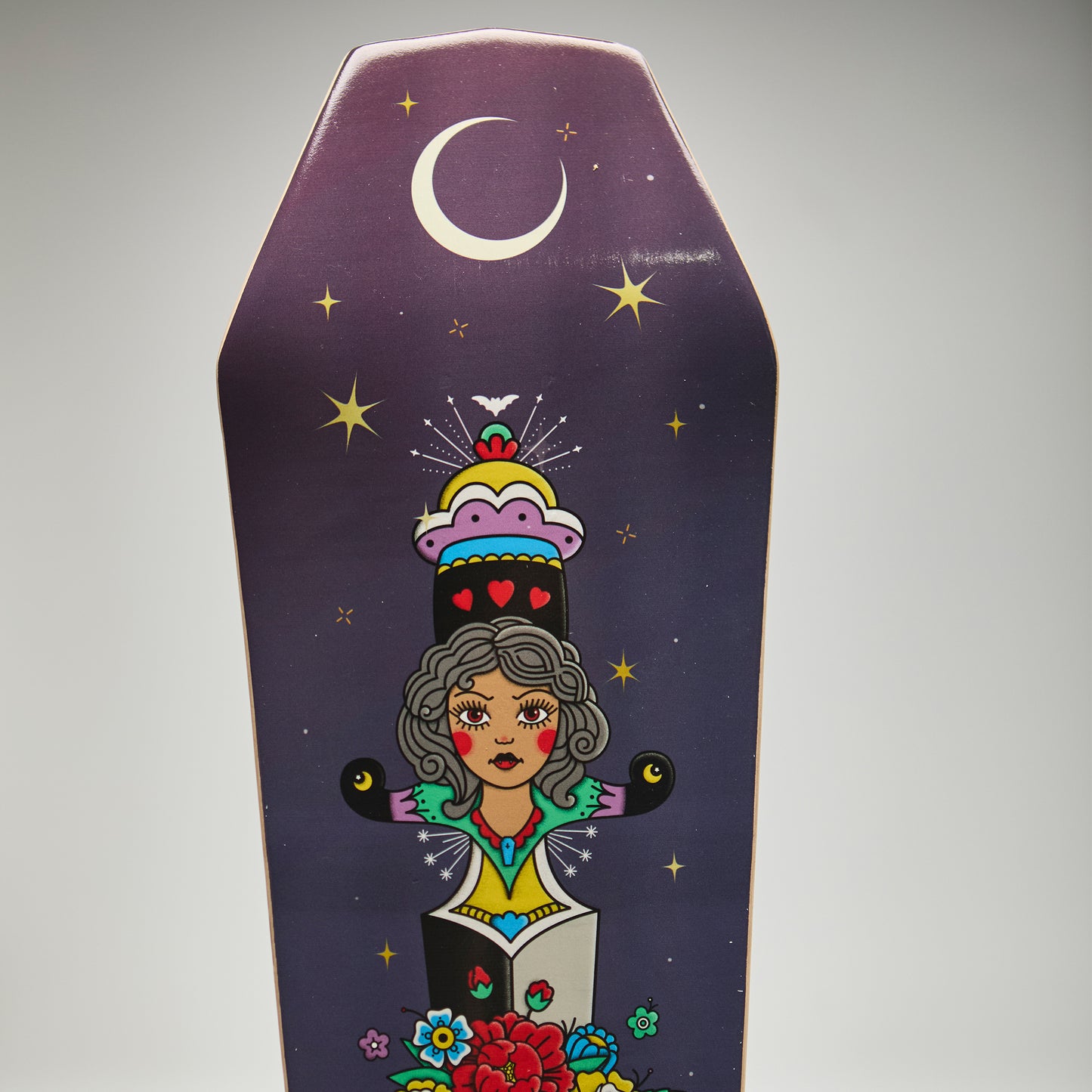 Decorative coffin-shaped skateboard deck with colorful illustration of a woman and celestial elements on a purple background.