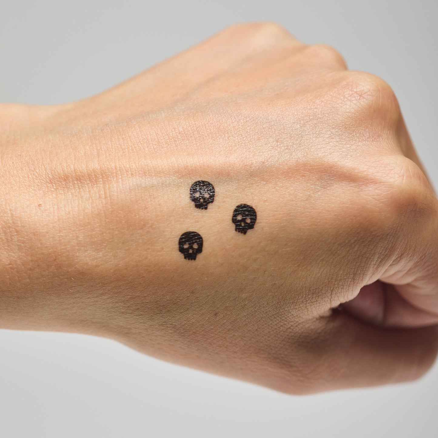 Three skull makeup stamps on a person's hand against a neutral background