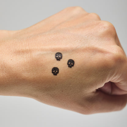 Three skull makeup stamps on a person's hand against a neutral background