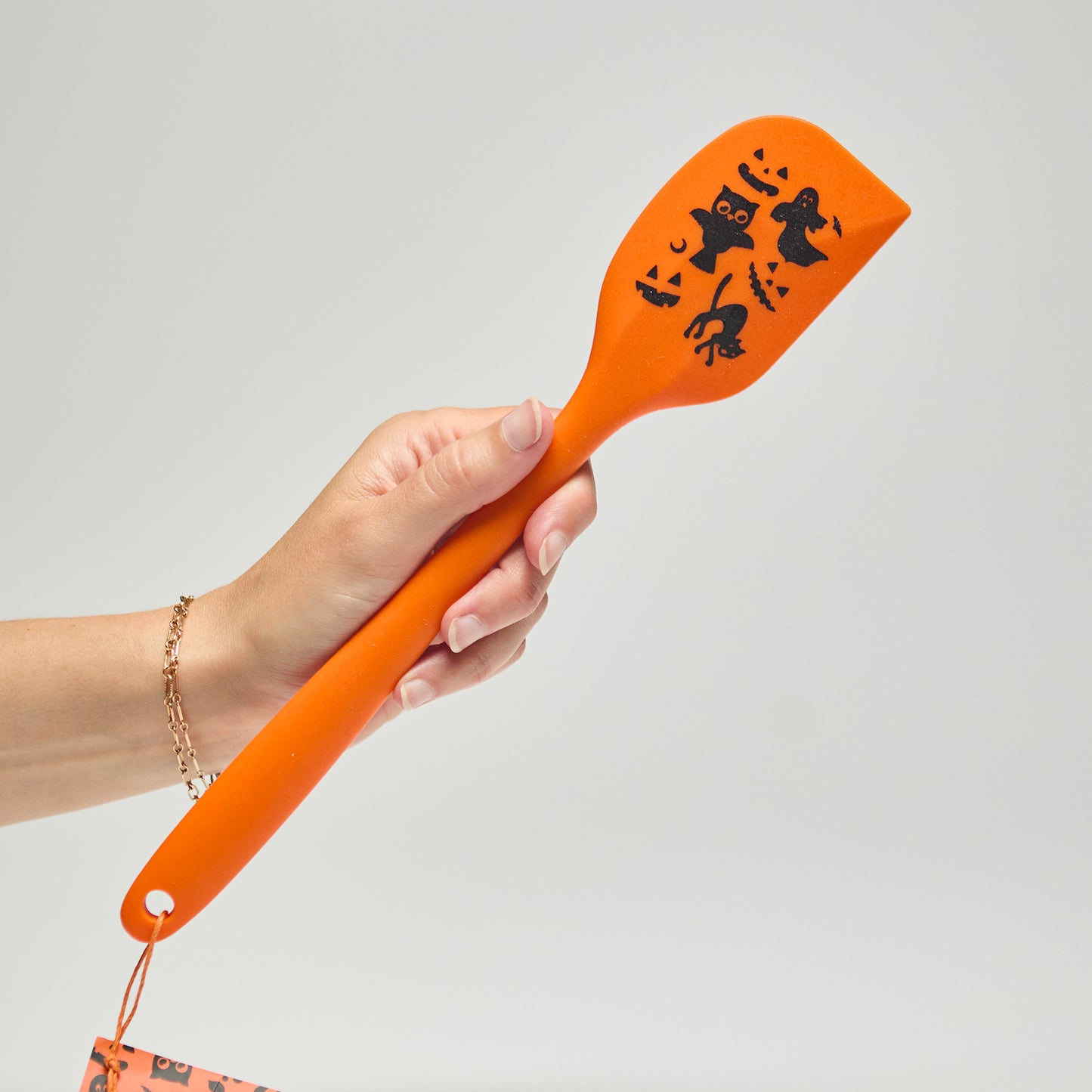 Hand holding an orange spatula with Halloween designs on a neutral background