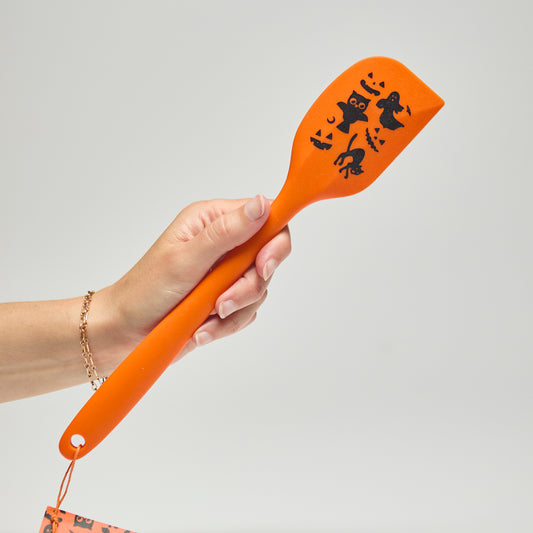 Hand holding an orange spatula with Halloween designs on a neutral background