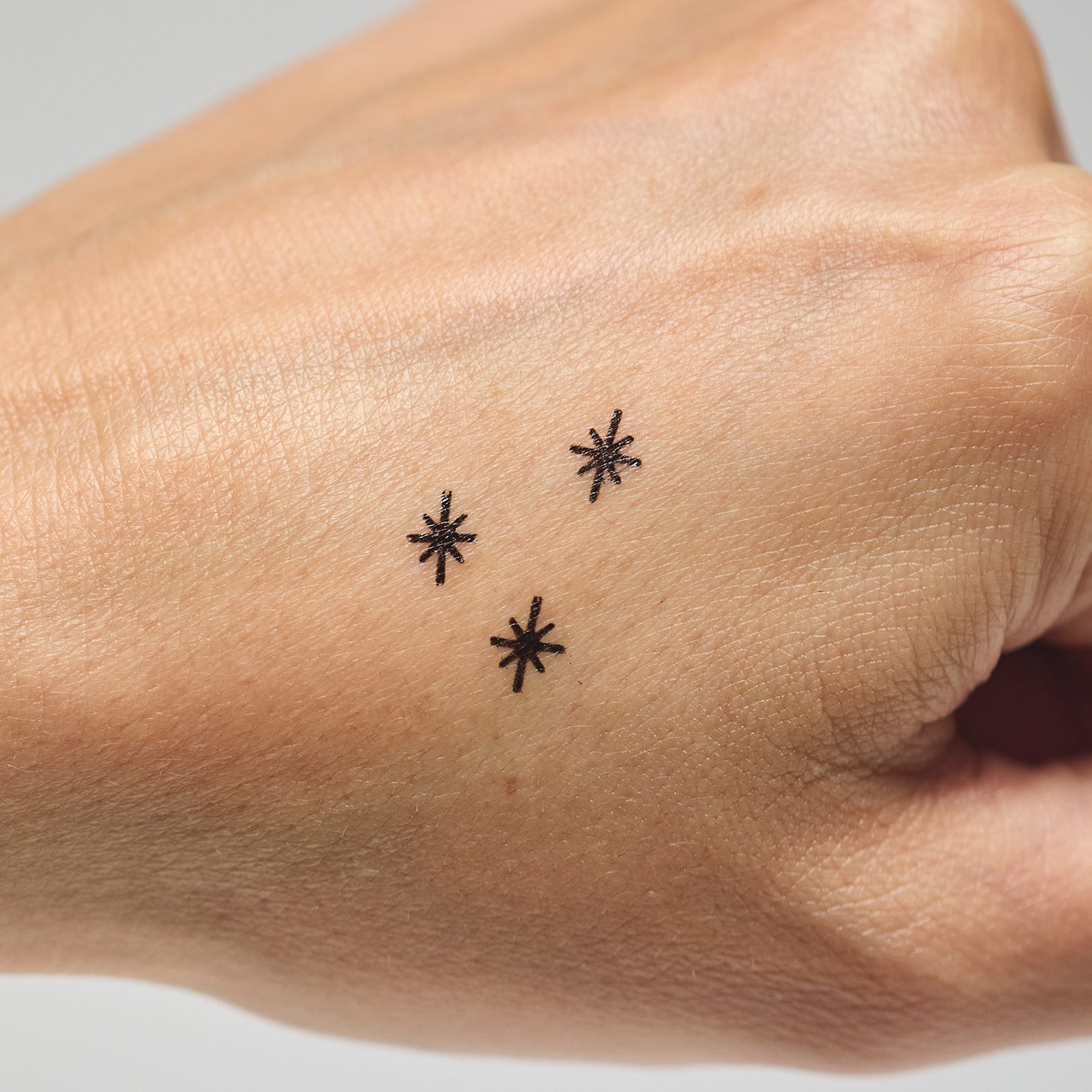 Three black star makeup stamps on a person's hand against a neutral background
