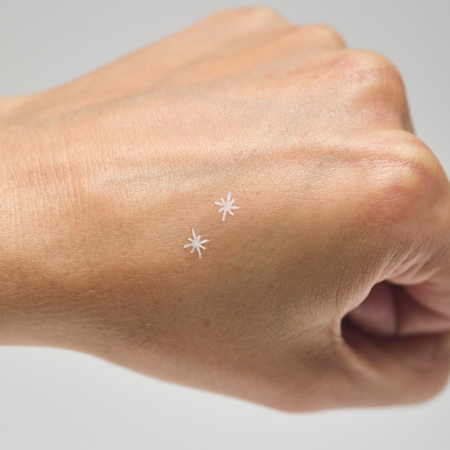 Two white star makeup stamps on a person's hand against a neutral background