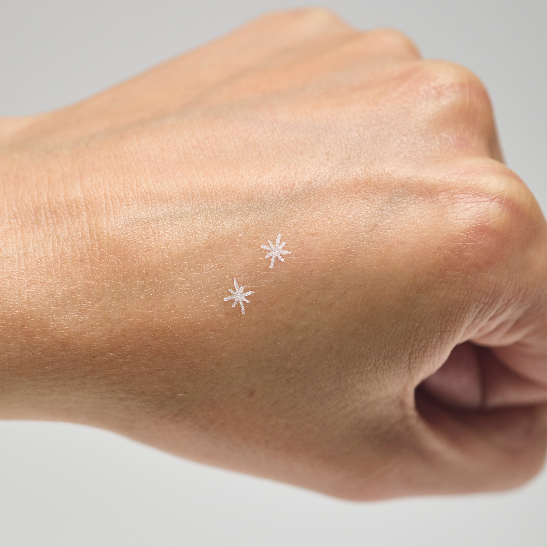 Two white star makeup stamps on a person's hand against a neutral background