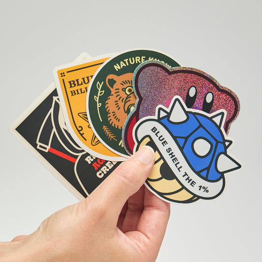 Hand holding a collection of colorful stickers with various designs on a light gray background