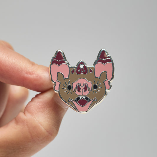 Enamel pin of a common vampire bat held by a hand against a neutral background