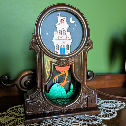 Decorative fireplace light with a Baba Yaga house design against a green background.