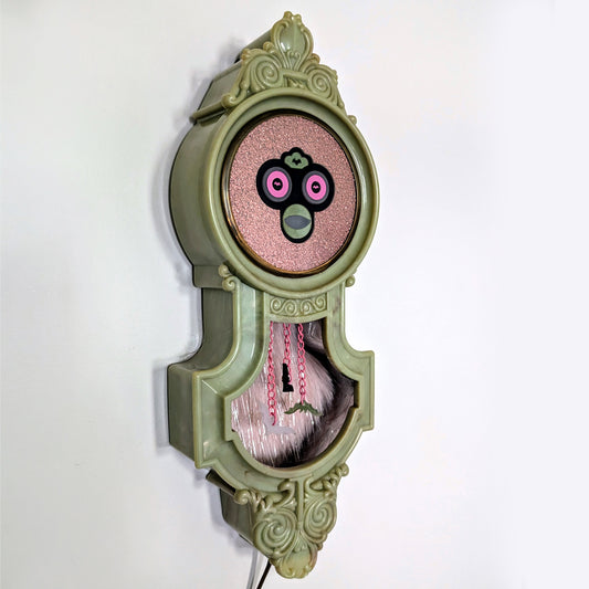 Hanging vintage clock frame with a Furby face and fur lining.