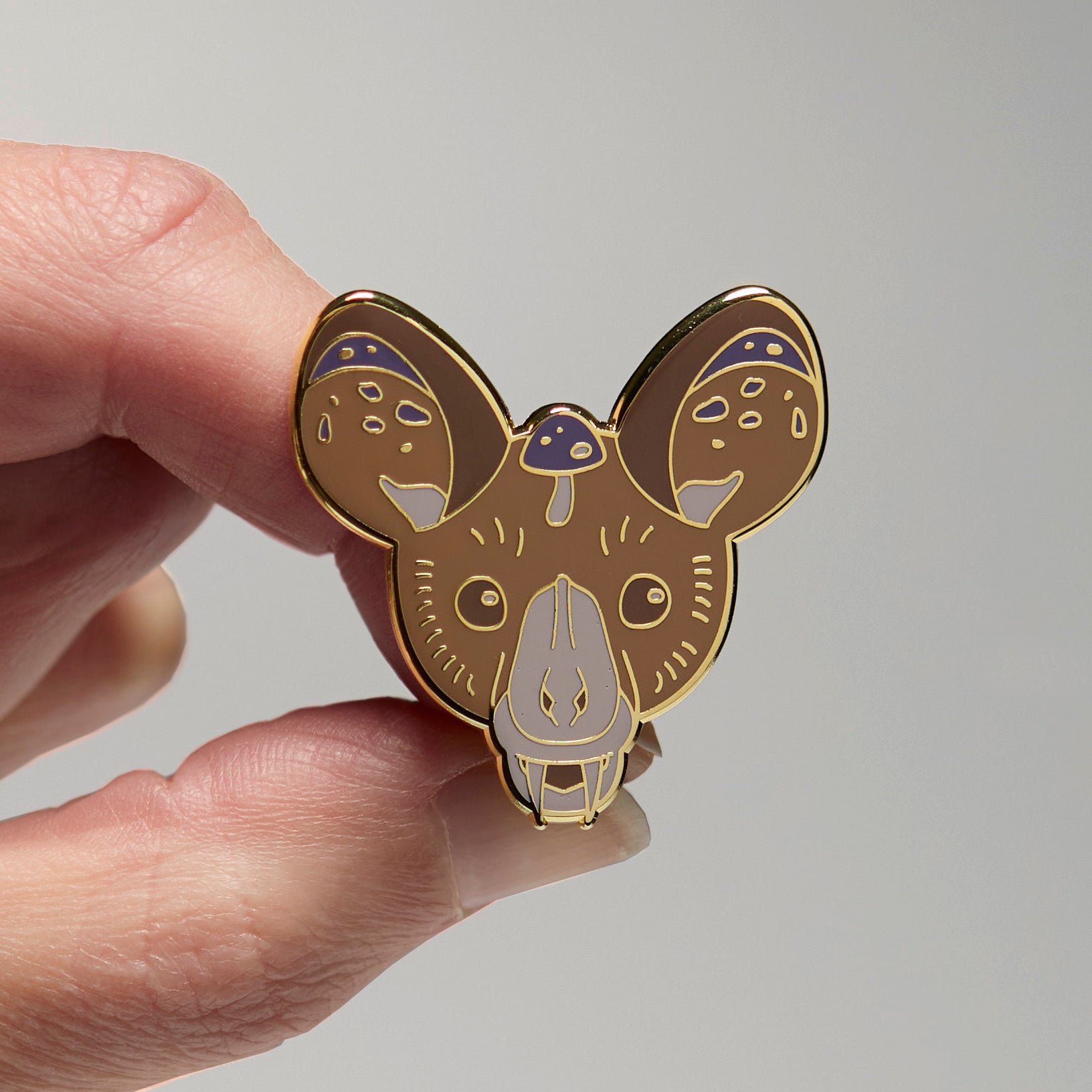 Enamel pin of a spectral bat held by a hand against a neutral background