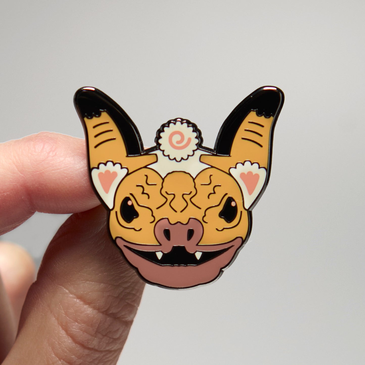 Enamel pin of a wrinkle-faced bat held by a hand against a neutral background