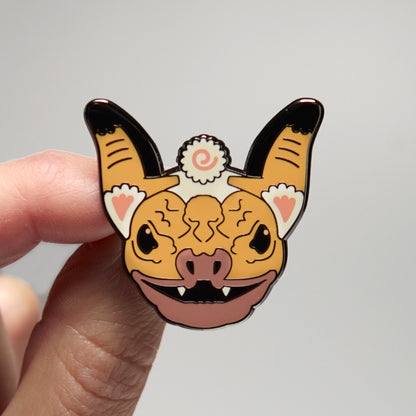 Enamel pin of a wrinkle-faced bat held by a hand against a neutral background