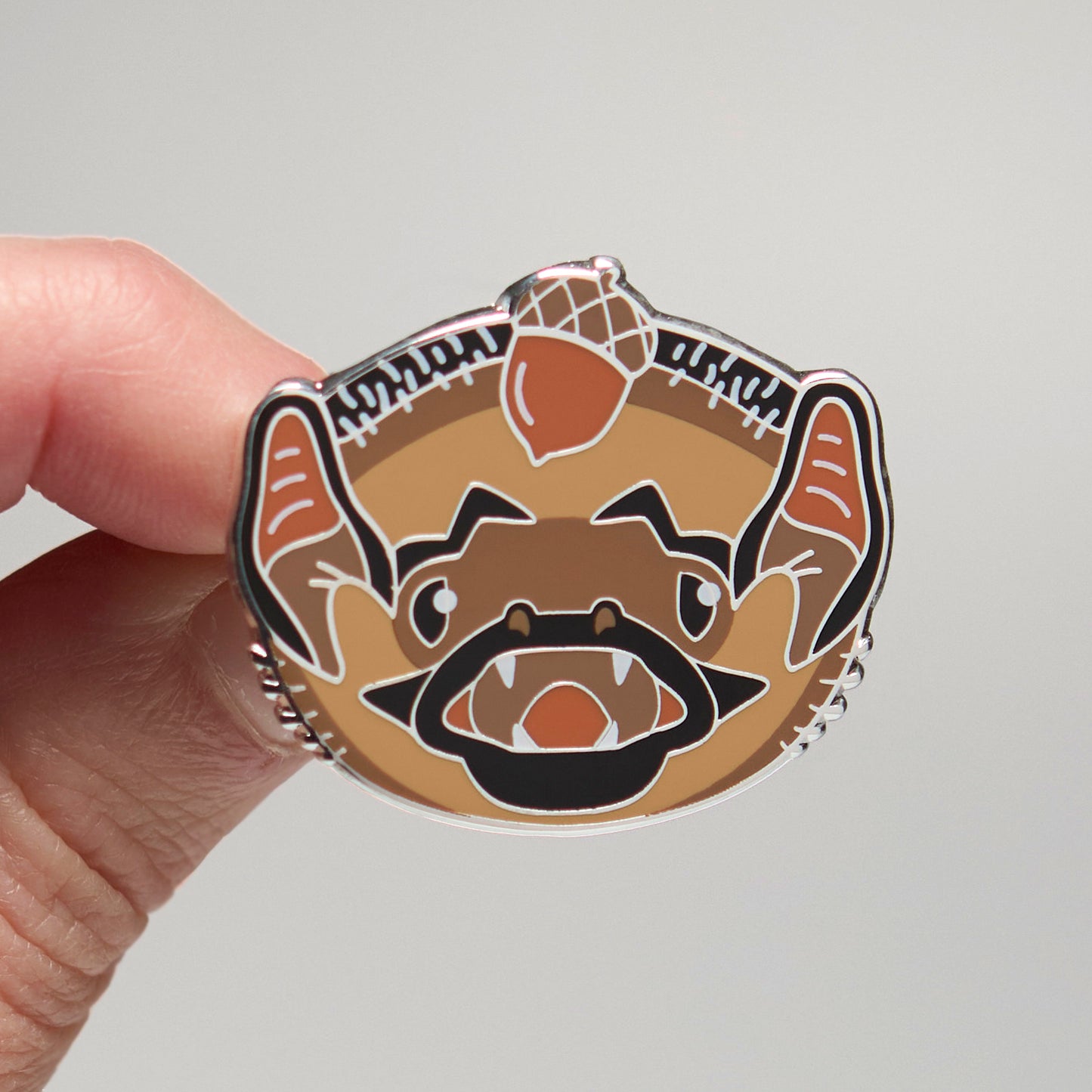 Enamel pin of a hoary bat held by a hand against a neutral background