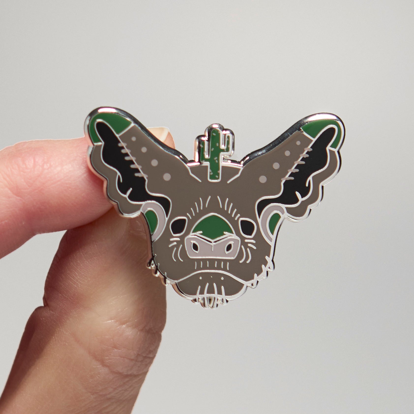 Enamel pin of a Mexican free-tailed bat held by a hand against a neutral background
