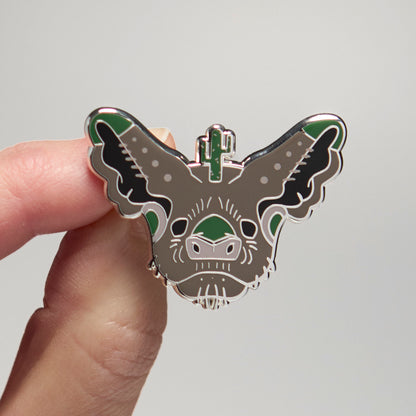 Enamel pin of a Mexican free-tailed bat held by a hand against a neutral background