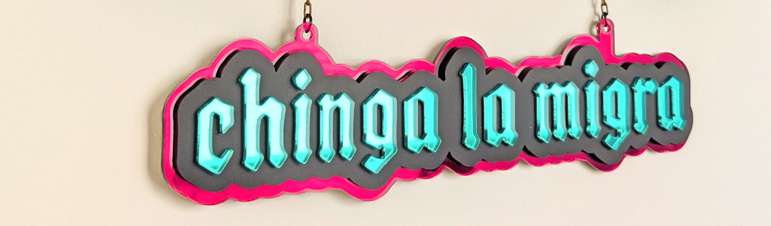 Red and green acrylic hanging sign that reads chinga la migra.