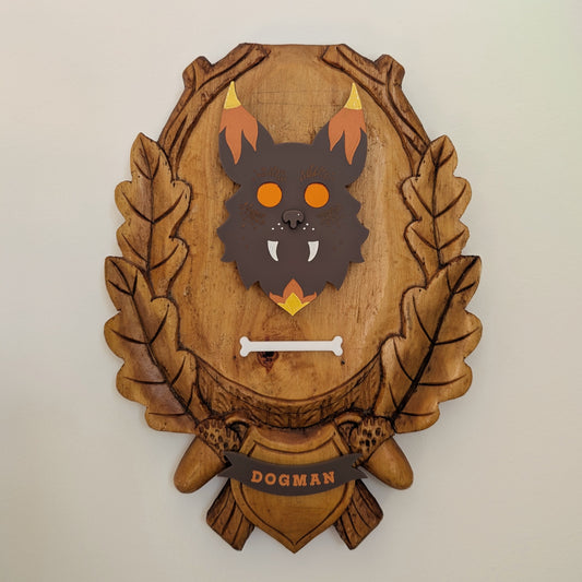 An acrylic Dogman head mounted on a wooden plaque hangs on a white wall.