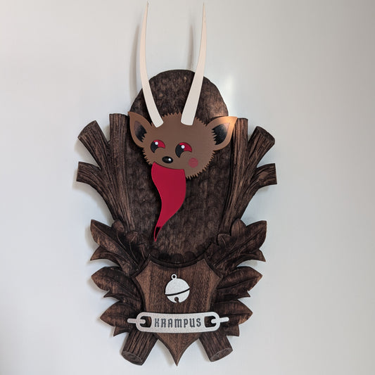 An acrylic Krampus head mounted on a wooden plaque hangs on a white wall.