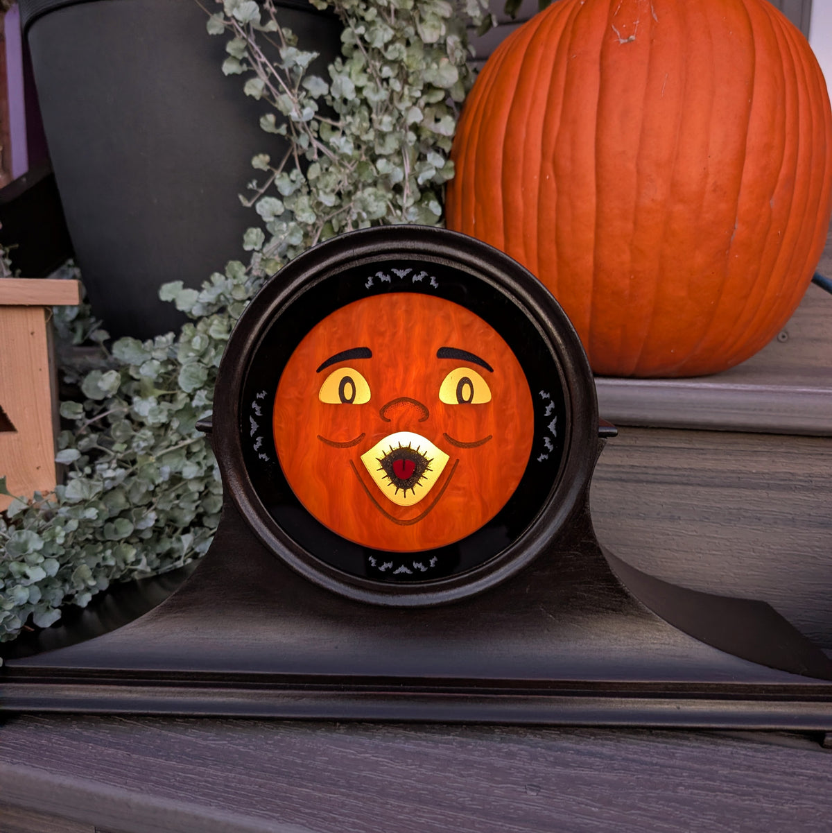 A vintage wood clock frame that has a jack-o-lantern for the face and is sitting on a step against a plants and pumpkins  The scene is dark with the face lit up from inside.