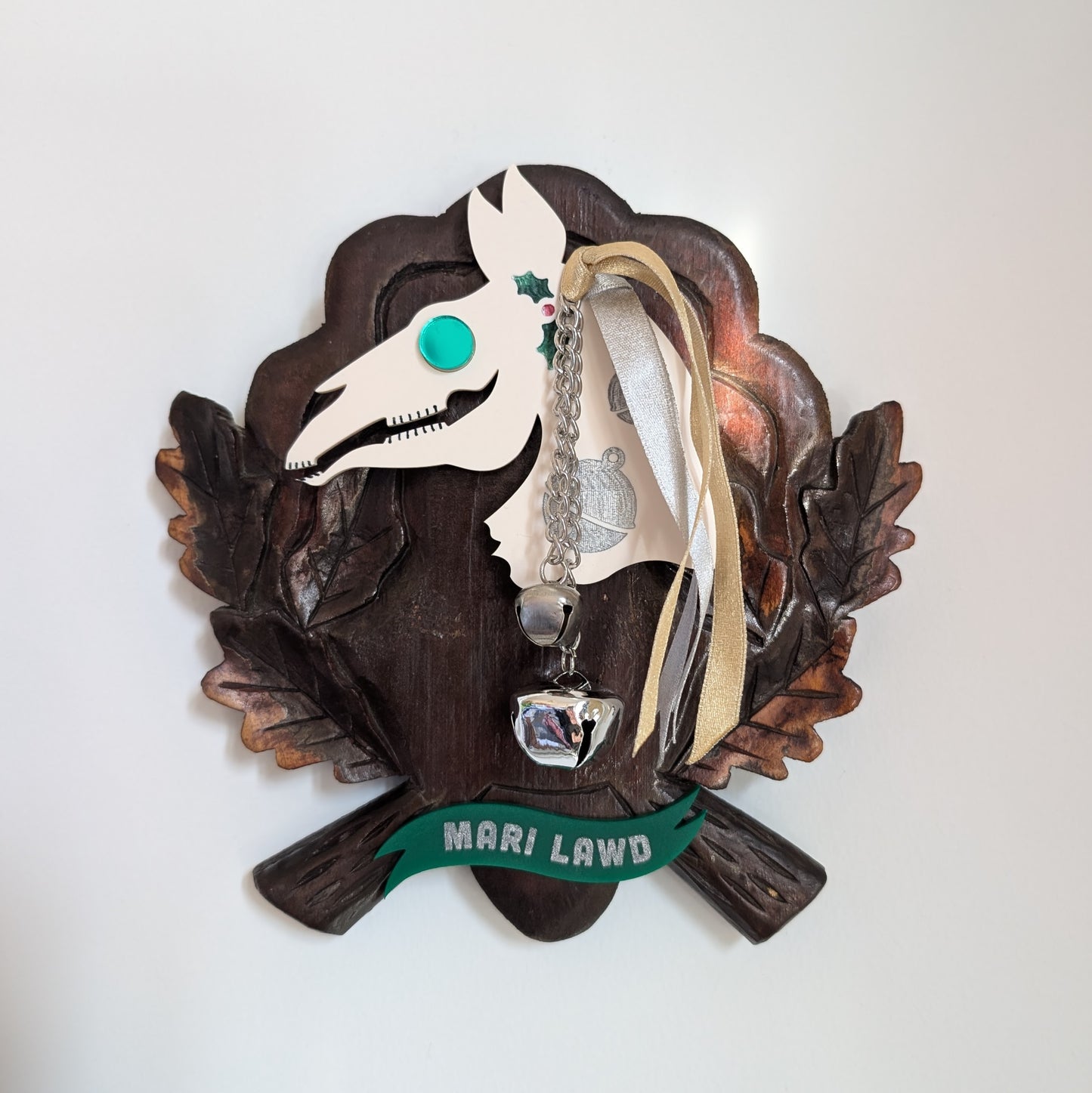 An acrylic Mari Lawd head mounted on a wooden plaque hangs on a white wall.