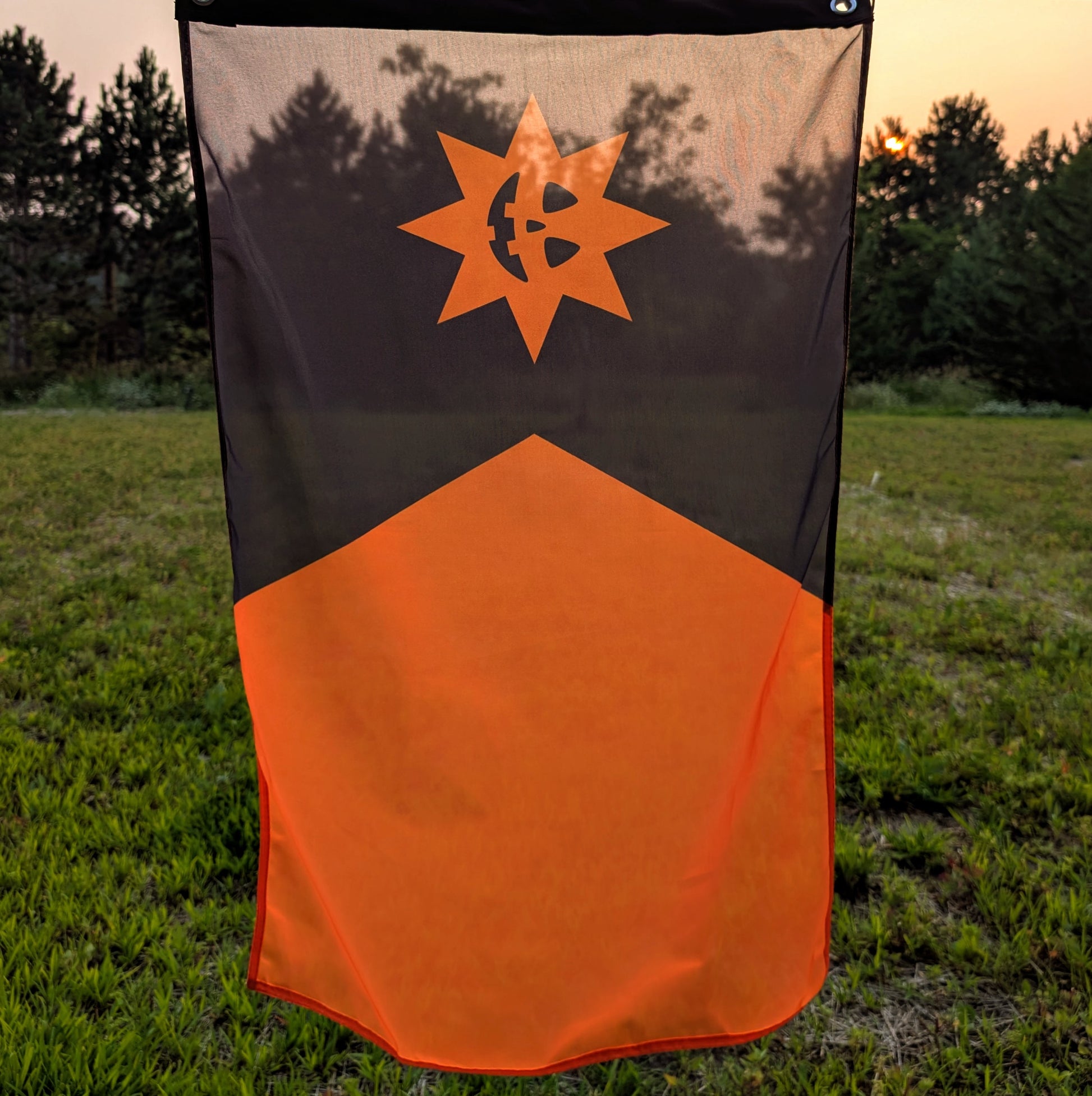 A black and orange Minnesota flag hanging in front of grass and trees during sunset.