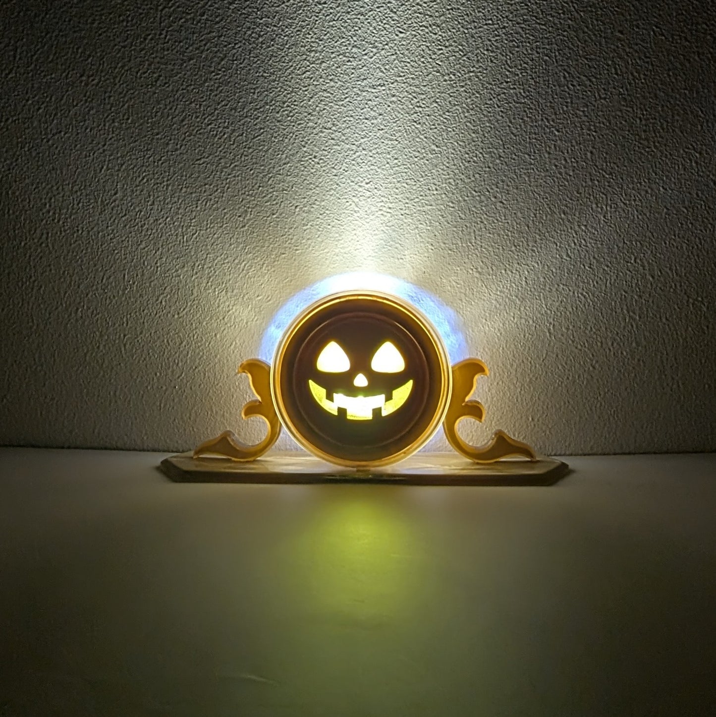 A vintage plastic clock frame repurposed with a yellow jack-o-lantern face. The light inside is turned on. 