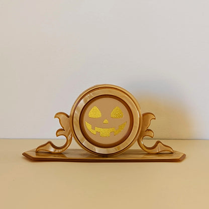 A vintage plastic clock frame repurposed with a yellow jack-o-lantern face. 