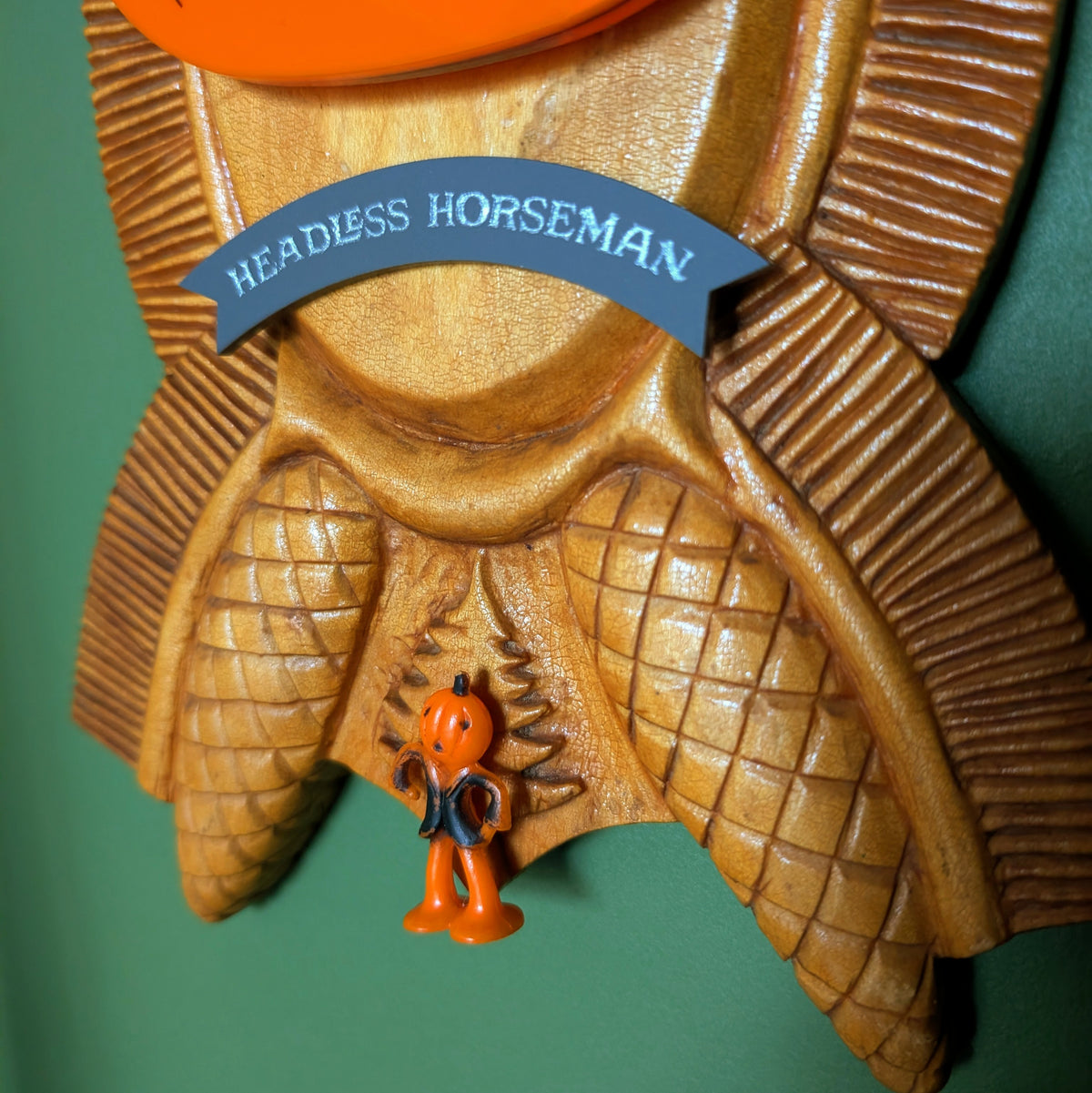 A closeup of the gray banner at the bottom of the carved wood plaque reads 'HEADLESS HORSEMAN' and a small pumpkin guy sits under it.