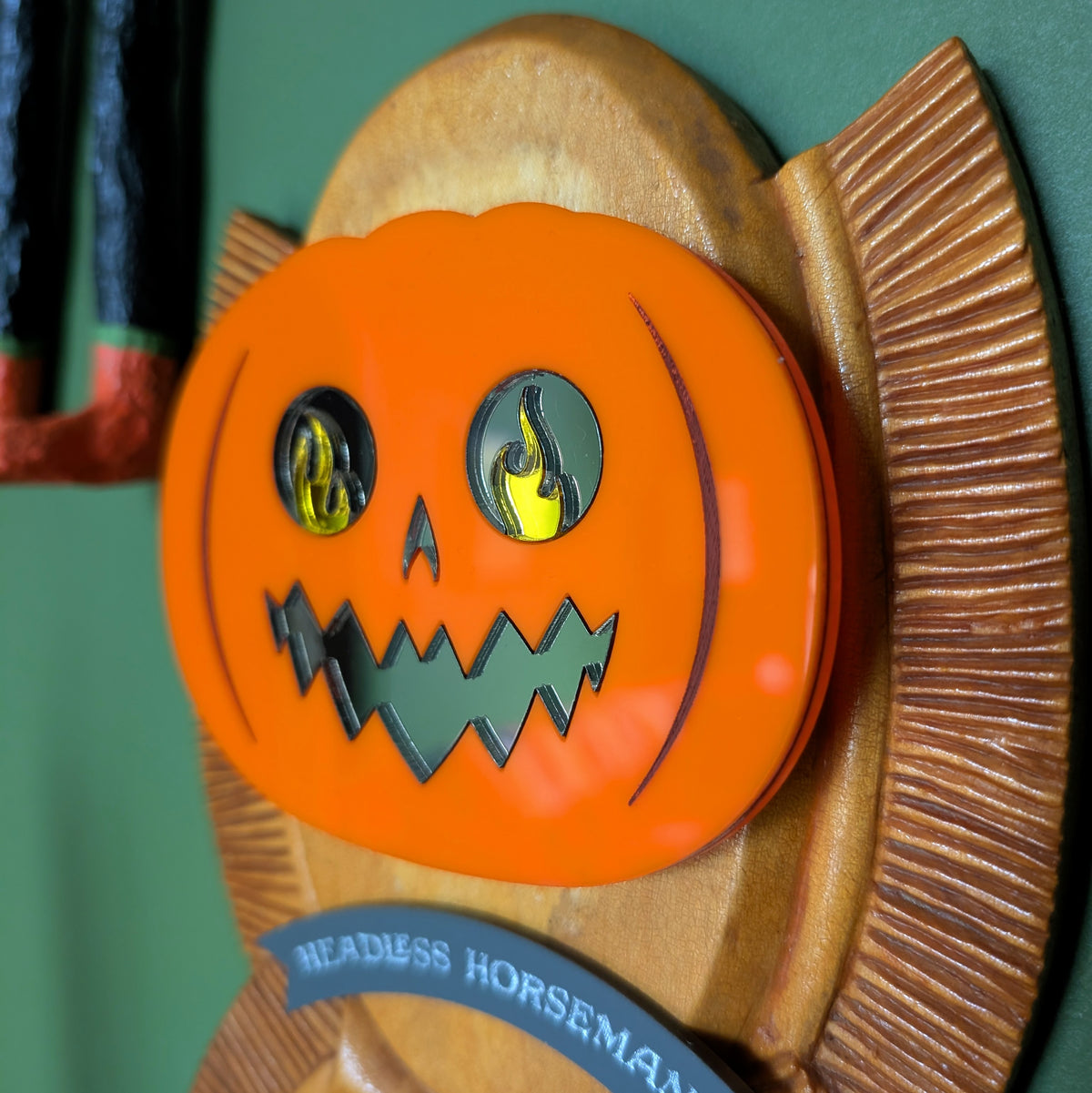 The closeup view of a vintage wooden carved wall plaque featuring an acrylic Headless Horseman with a mirror face against a green background. 