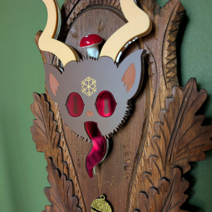 A closeup view of a vintage wooden carved wall plaque featuring an acrylic Krampus head with red mirror eyes and tongue, a vintage mushroom, and a gold bell accent. 