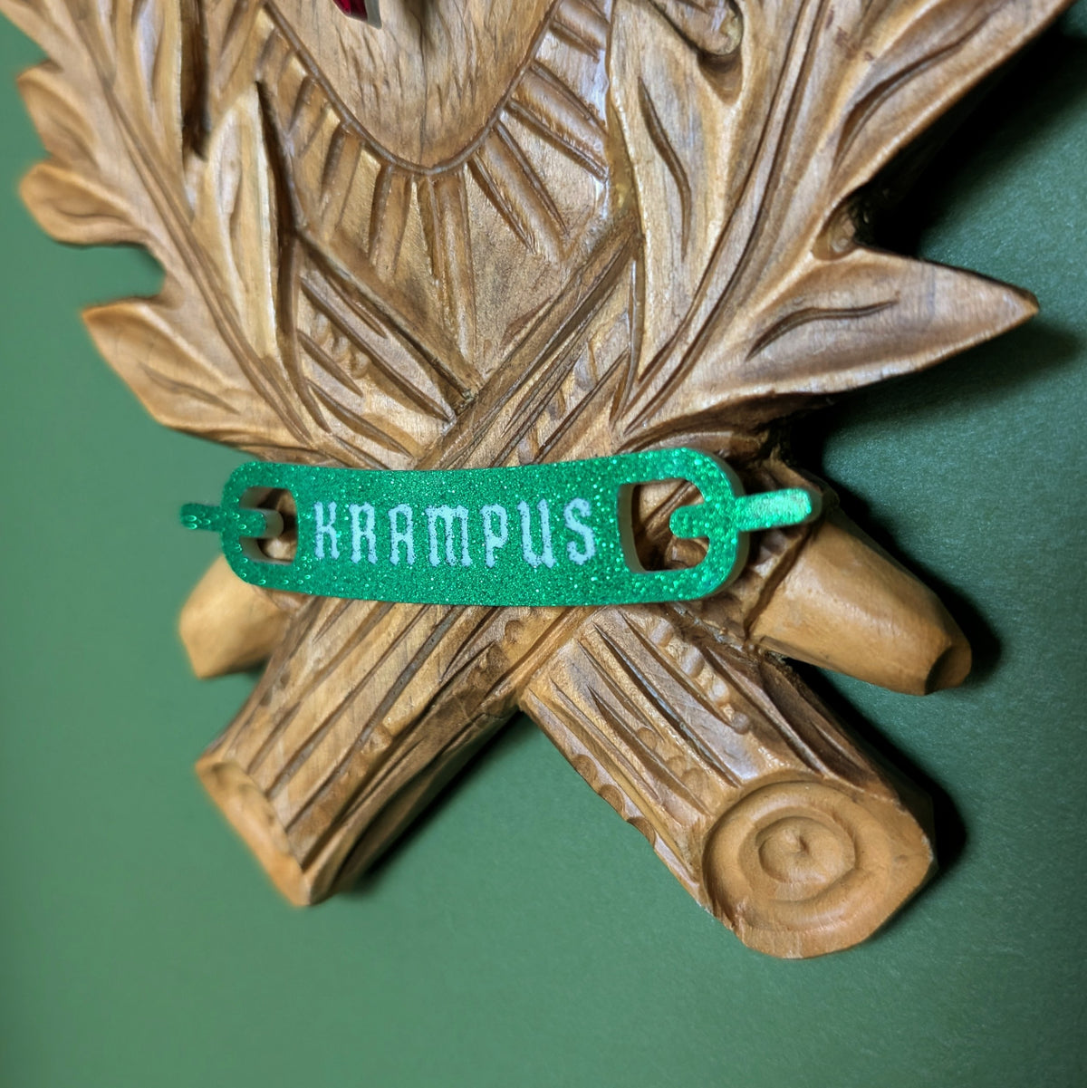 A closeup of the green glitter banner at the bottom of the carved wood plaque reads 'KRAMPUS.