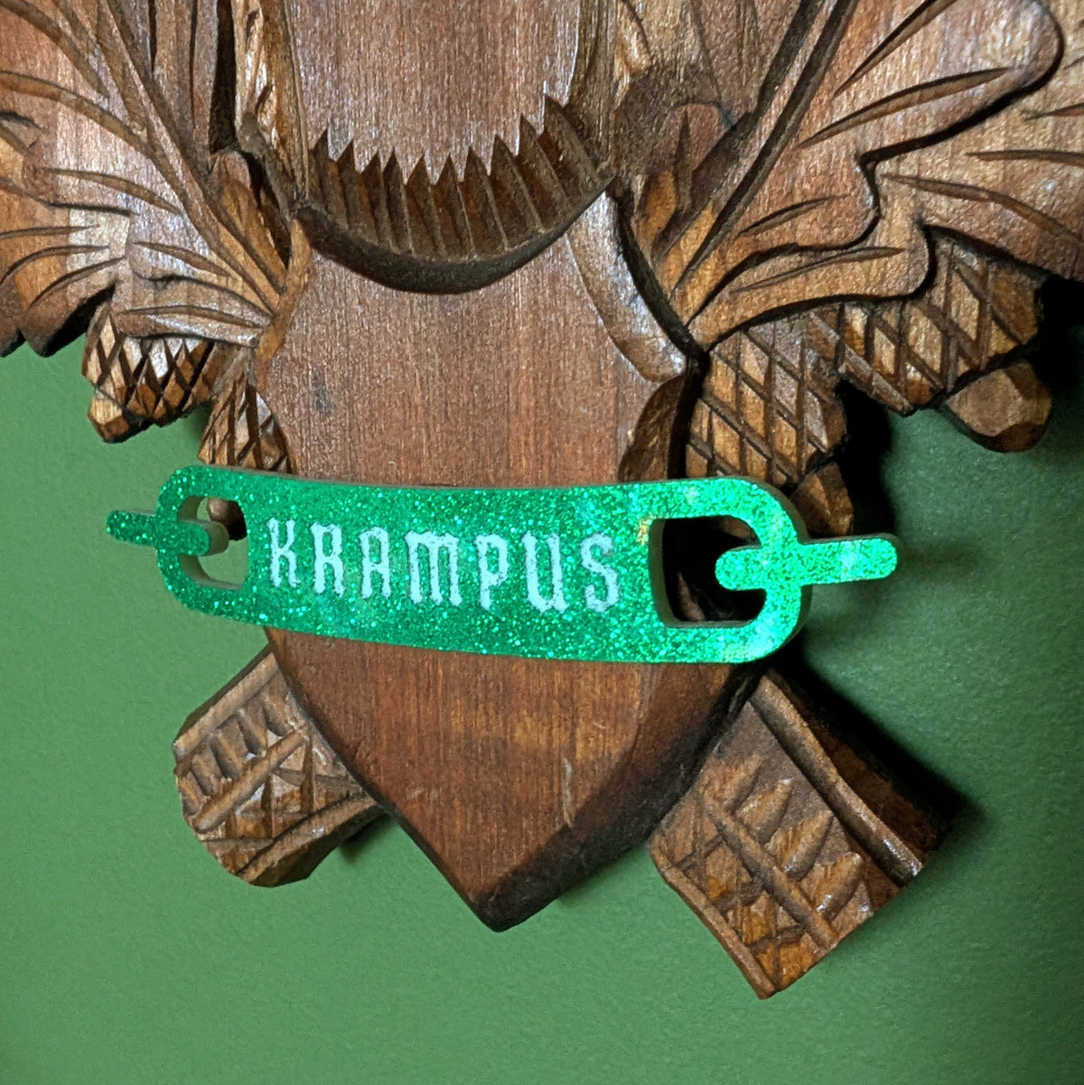A closeup of the green glitter banner at the bottom of the carved wood plaque reads 'KRAMPUS.