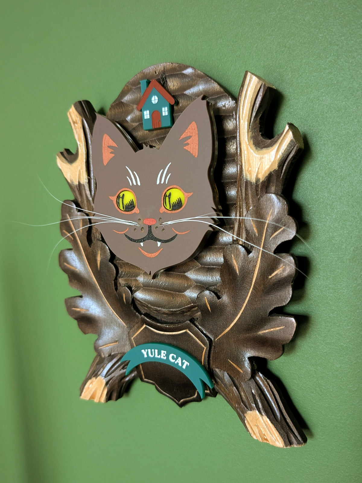 A vintage wooden carved wall plaque featuring an acrylic yule cat with large yellow eyes and a small house accent. A teal banner at the bottom reads 'YULE CAT'.