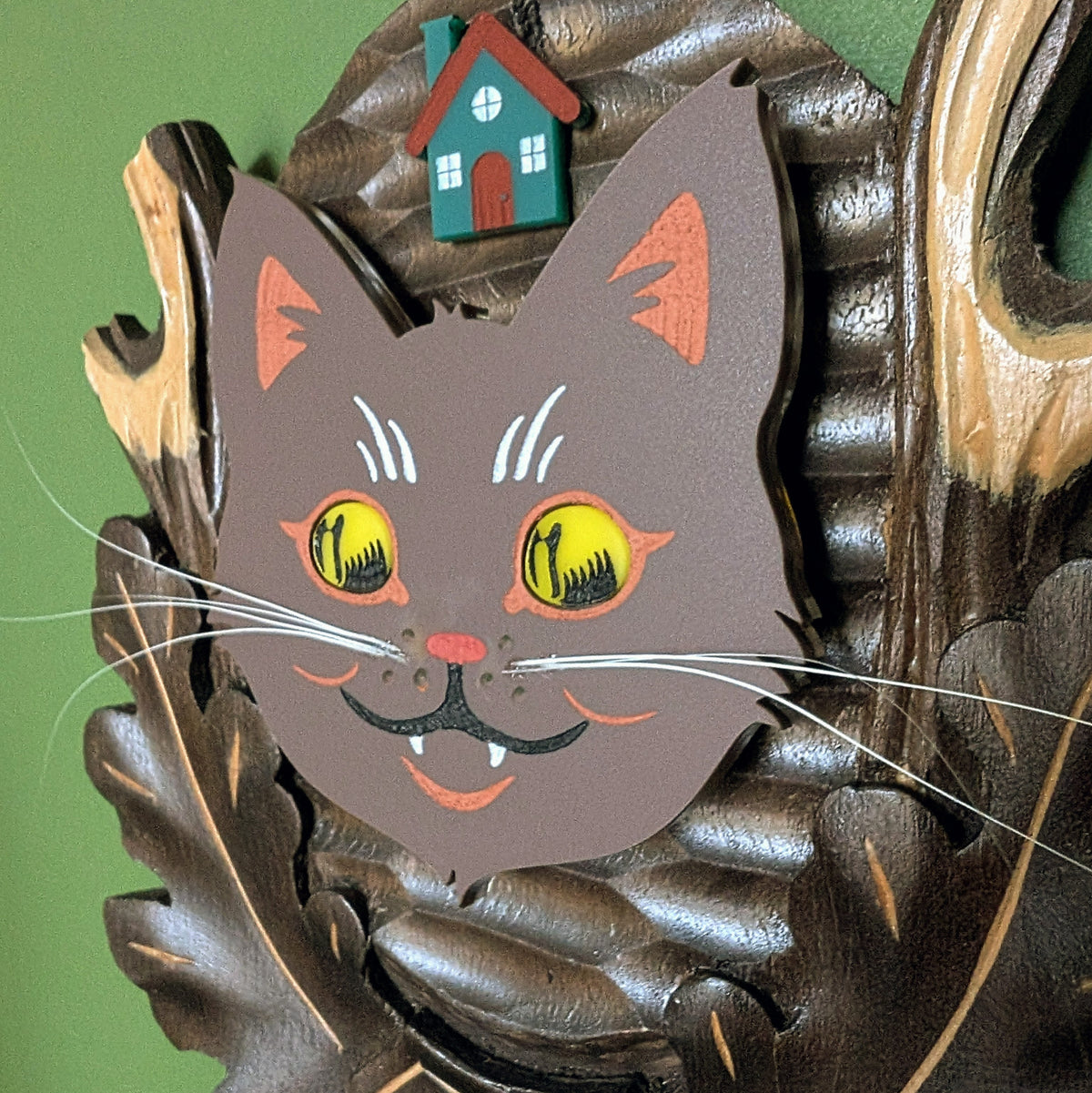 A closeup of a vintage wooden carved wall plaque featuring an acrylic yule cat with large yellow eyes , real cat whiskers, and a small house accent. 